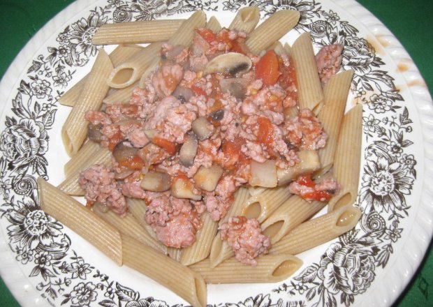 Fotografia przedstawiająca brazowy makaron z sosem pomidorowym i pieczarkami