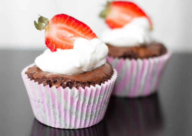 Fotografia przedstawiająca Brownie czyli mega czekoladowa muffinka z bitą śmietaną i truskawkami