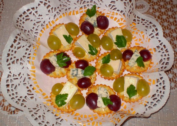 Fotografia przedstawiająca Camembert i Roquefort na krakersach z winogronami :