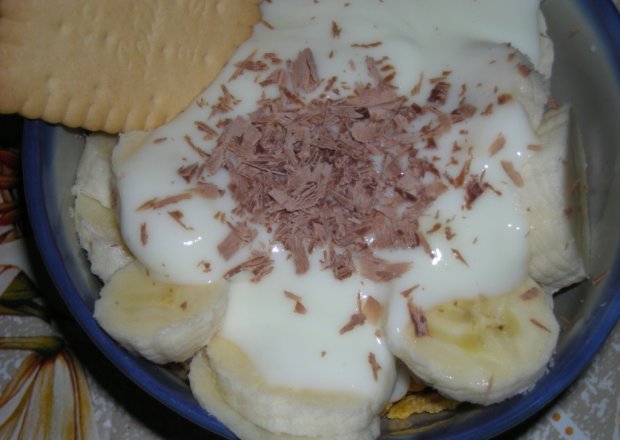 Fotografia przedstawiająca deser jogurtowy z bananami i p,łatkami kukurydzianymi