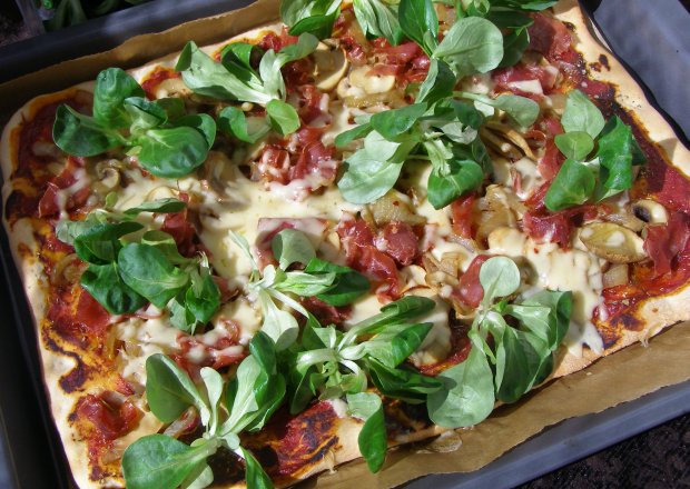 Fotografia przedstawiająca domowa pizza z roszponką i szynką serrano...