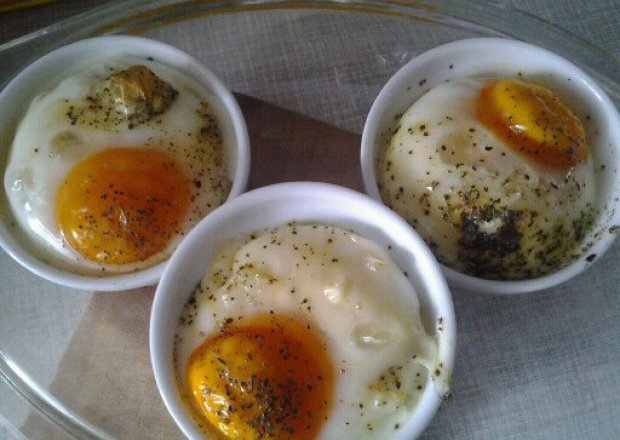 Fotografia przedstawiająca jajka w kokilkach z dodatkami.