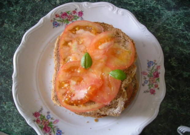 Fotografia przedstawiająca kanapki z masełkiem czosnkowym, pomidorem i bazylią
