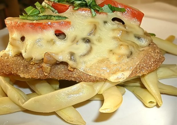 Fotografia przedstawiająca Kotlet schabowy zapieczony pod pieczarkami, pomidorem i serem.