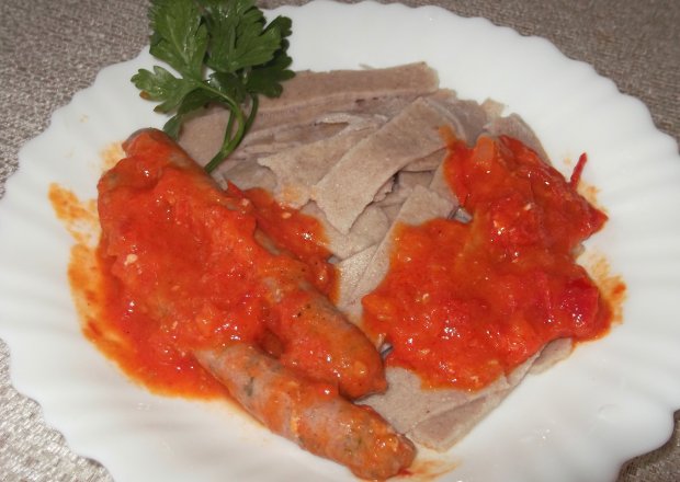 Fotografia przedstawiająca Makaron gryczany z białymi kiełbaskami w sosie pomidorowym.