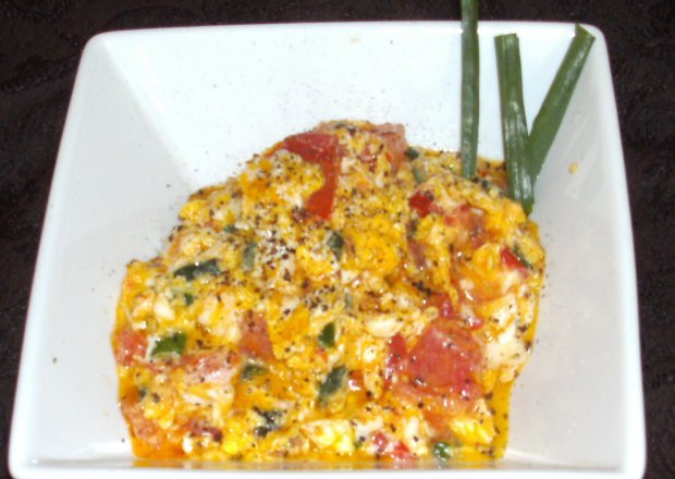 Fotografia przedstawiająca na maśle z pomidorami,szczypiorkiem śniadaniowa jajecznica...