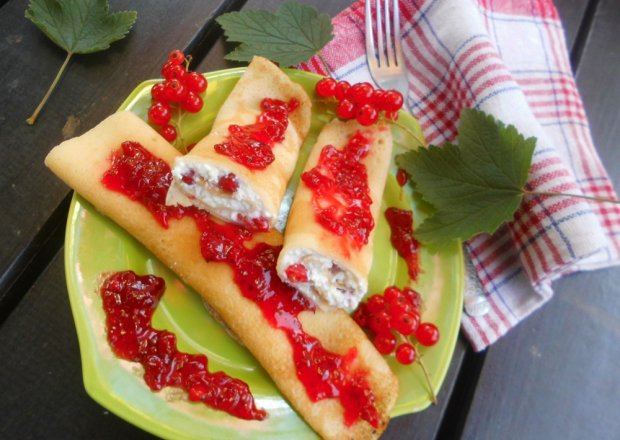 Fotografia przedstawiająca Naleśniki z serem i czerwonymi porzeczkami polane sosem porzeczkowym.