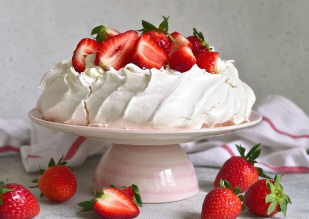 Fotografia przedstawiająca Pavlova z truskawkami i sosem truskawkowym