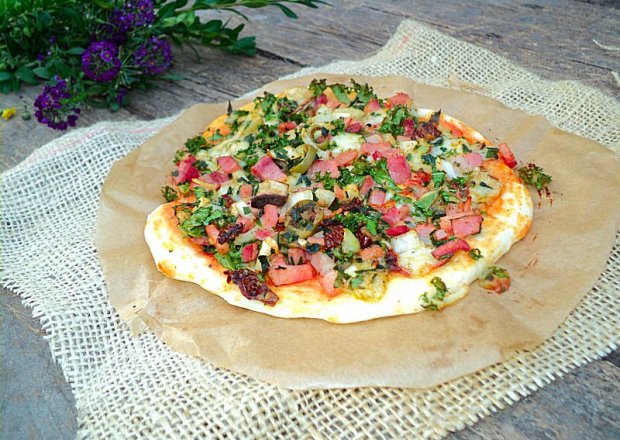 Fotografia przedstawiająca Pizza na cienkim cieście z jarmużem, boczkiem, suchą kiełbasą i mozzarellą