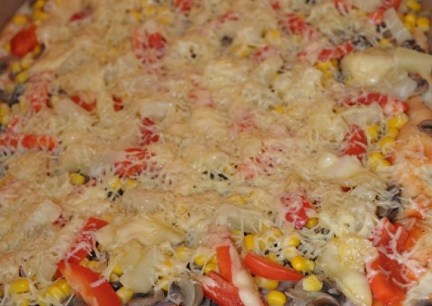 Fotografia przedstawiająca pizza z ananasem, kukurydzą, pieczarkami, cebulą, papryką, wędliną i serem.