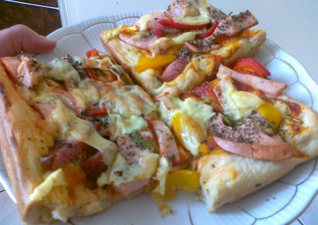 Fotografia przedstawiająca pizza z szynką i czeerwoną i żółtą papryką