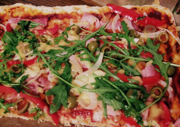 Fotografia przedstawiająca Pizza z szynką, oliwkami, papryką i rukolą