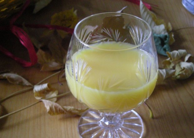 Fotografia przedstawiająca pomarańczowy drink z szampanem i musem truskawkowym
