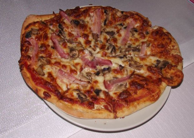 Fotografia przedstawiająca Rumiana pizza z mozzarellą, pieczarkami i boczkiem na ziołowym spodzie