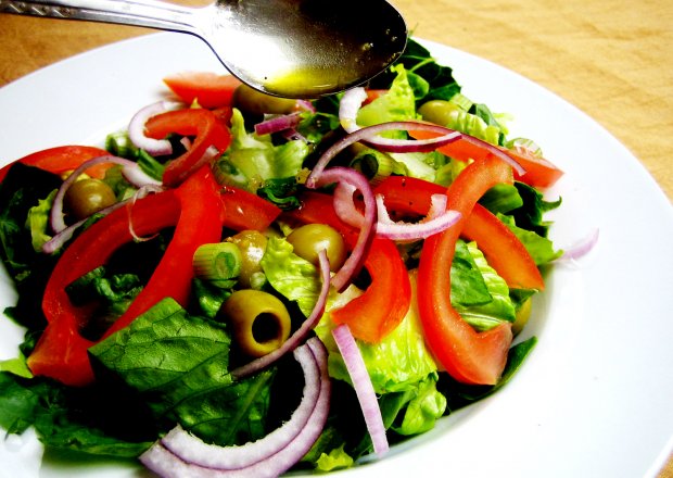 Fotografia przedstawiająca sałatka z oliwkami, pomidorem i czerwoną cebulą z dressingiem cytrusowym