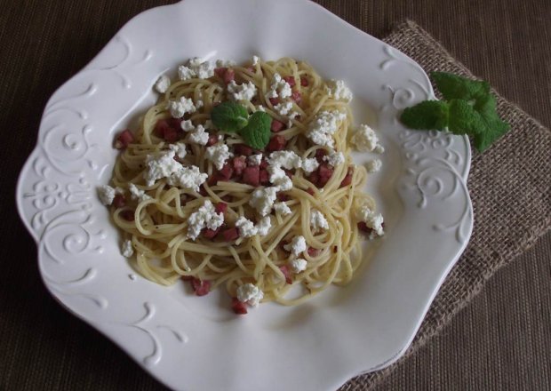 Fotografia przedstawiająca Spaghetti z kiełbasą smażoną z cebulą podane z białym serem
