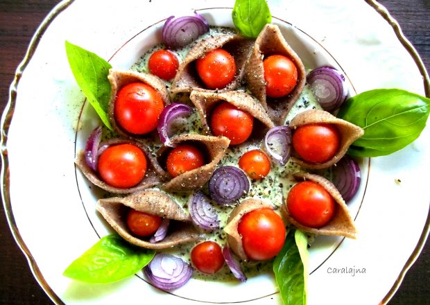 Fotografia przedstawiająca wesoła sałatka z makaronem muszelki nadziewanymi pomidorkami i pływającymi w bazyliowym jogurcie