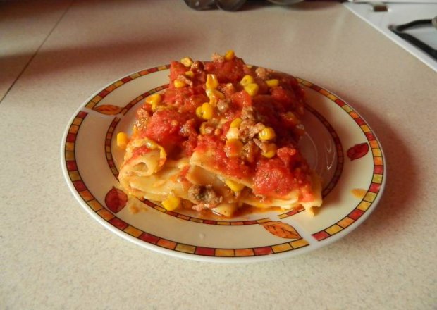 Fotografia przedstawiająca Zapiekane cannelloni nadziane mięsem mielonym i kukurydzą w sosie pomidorowym.
