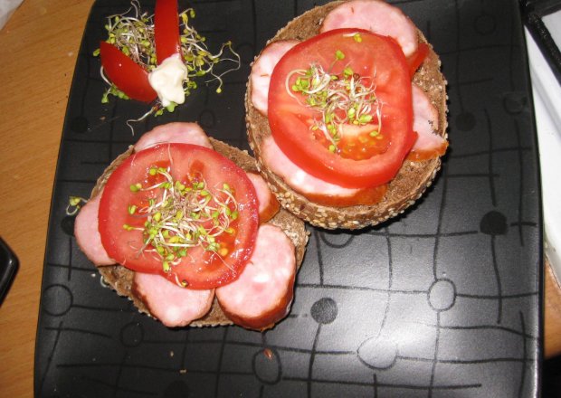 Fotografia przedstawiająca ziarnista bułka z kiełbasą i pomidorem